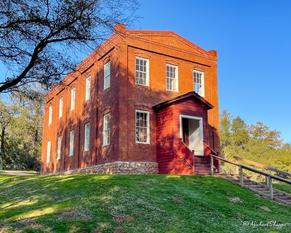 The historic Columbia schoolhouse, a two-story red brick building on a grassy hill