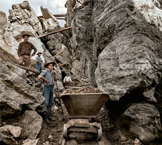 Gold Rush era miners working in a rocky quarry with wheelbarrows and timber scaffolding