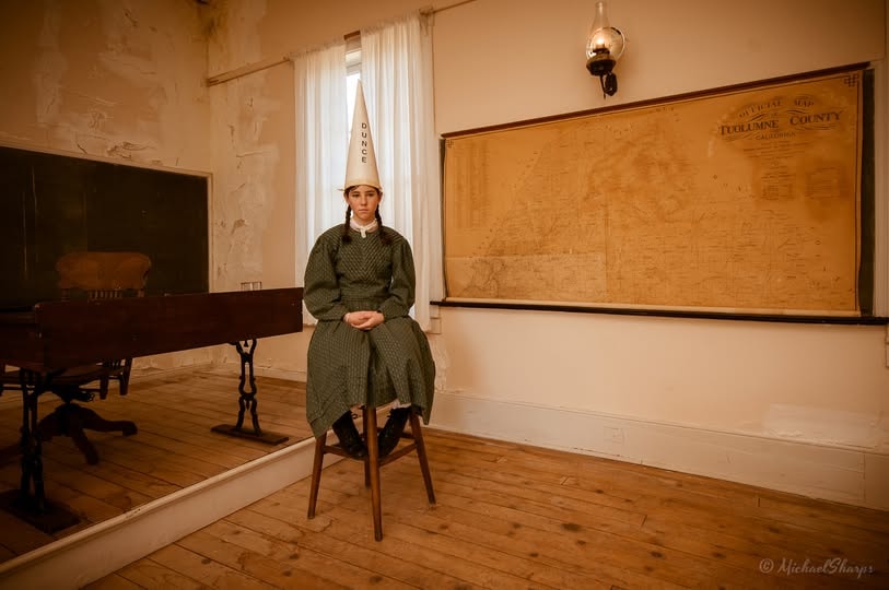 Period-costumed student in dunce cap in the historic Columbia schoolhouse